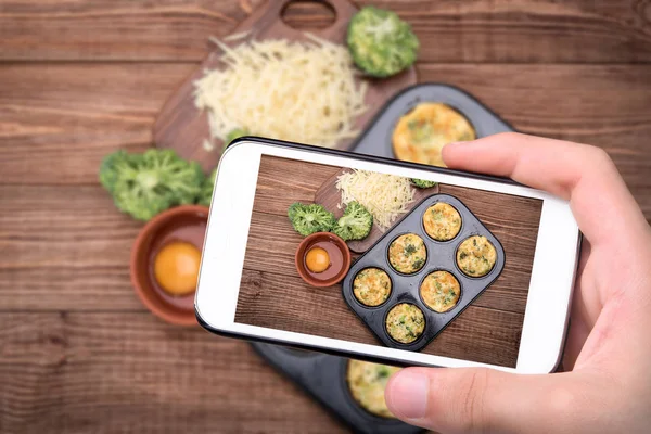 Mani che scattano foto muffin all'uovo broccoli e formaggio con smartphone . — Foto Stock