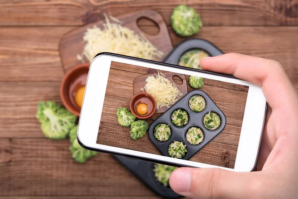 Händer som tar foto ägg muffins broccoli och ost med smartphone. — Stockfoto