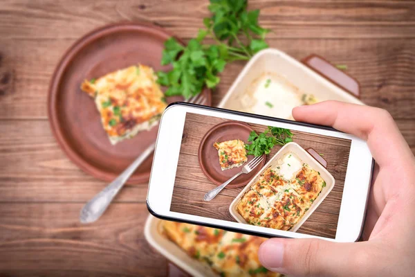 Mãos tirando foto lasanha de frango e queijo branco com smartphone . — Fotografia de Stock