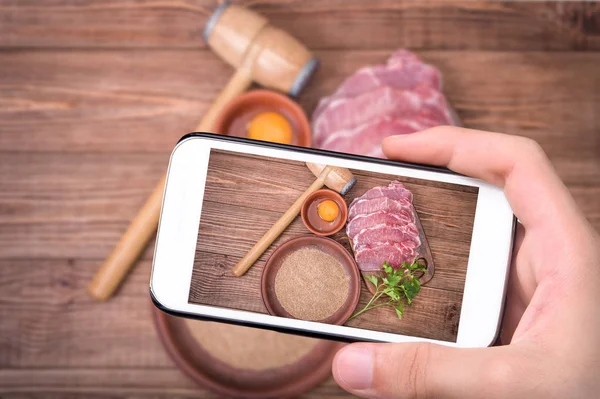 Mãos tirando foto schnitzel de porco cru com smartphone . — Fotografia de Stock