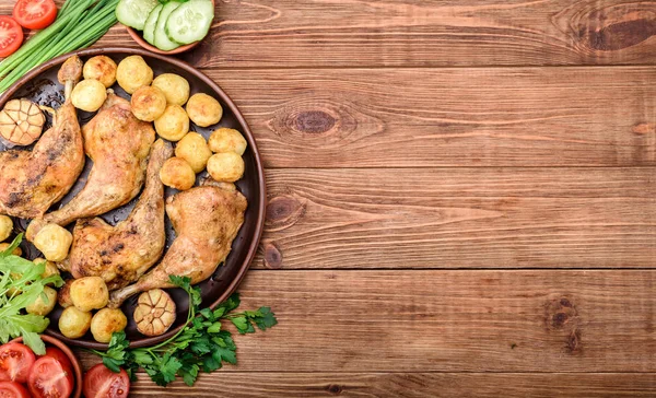 Pernas de frango com batatas assadas e legumes no fundo de madeira . — Fotografia de Stock