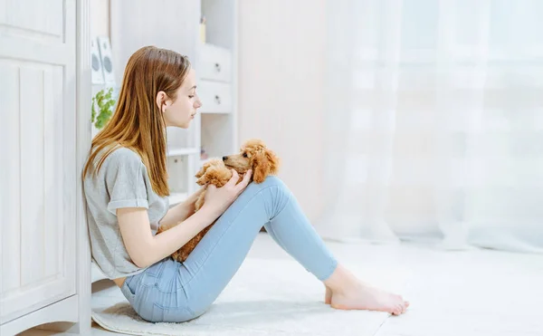 Giovane ragazza sta riposando con un cane sul pavimento a casa  . — Foto Stock