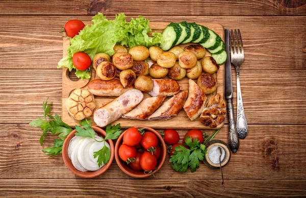 Sosis panggang dan sayuran di papan kayu . — Stok Foto
