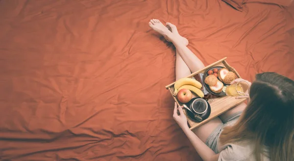 La jeune femme est couchée au lit et prend un petit déjeuner sain . — Photo