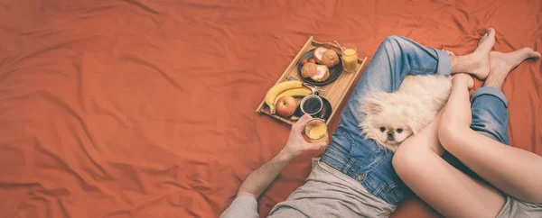 Jeune couple est couché au lit avec un chien et prendre un petit déjeuner sain . — Photo