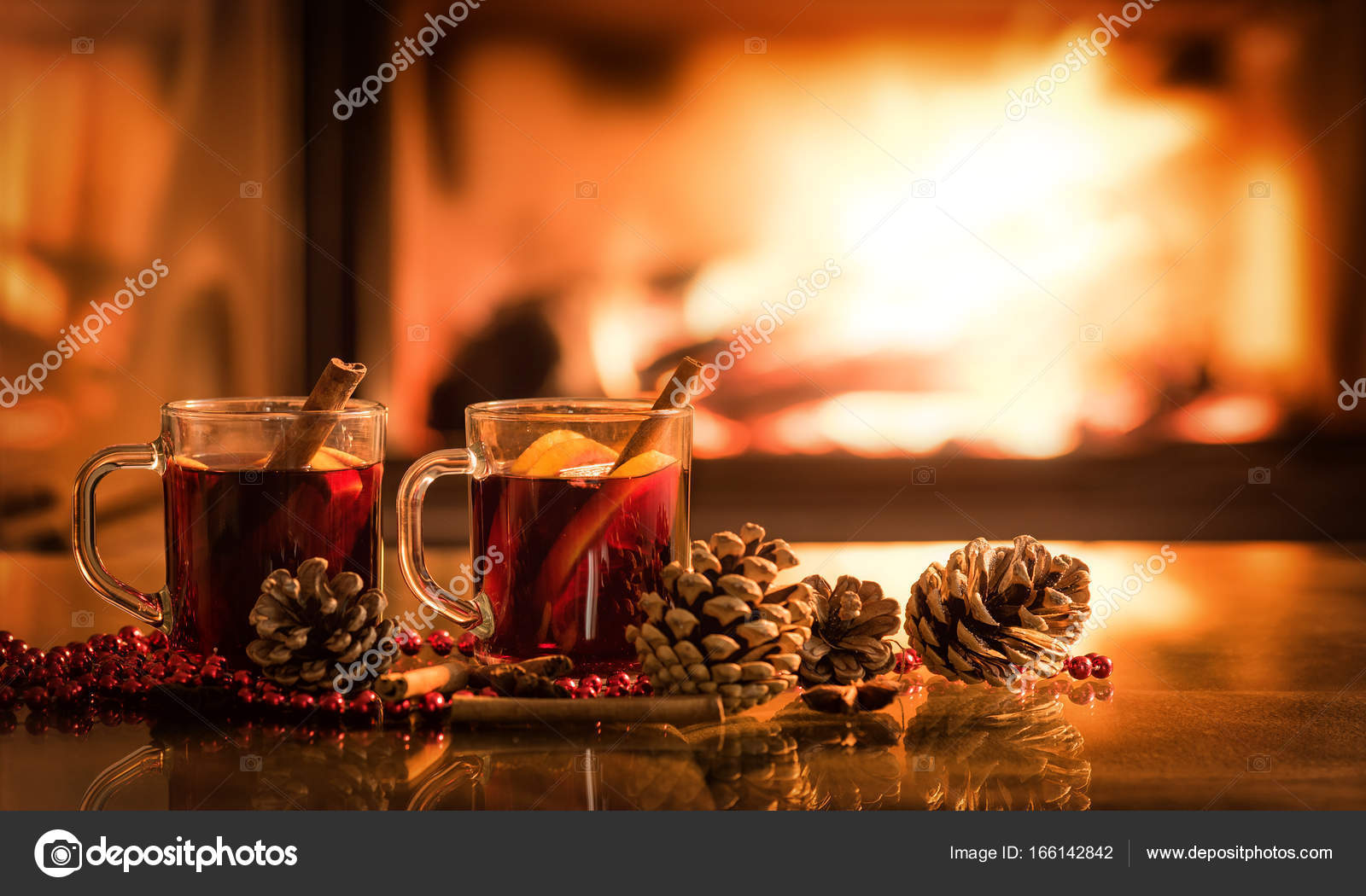 Mulled wine glasses on table in front of burning fireplace. Stock