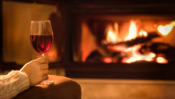 Junge Frau sitzt zu Hause am Kamin und trinkt einen Rotwein. — Stockfoto