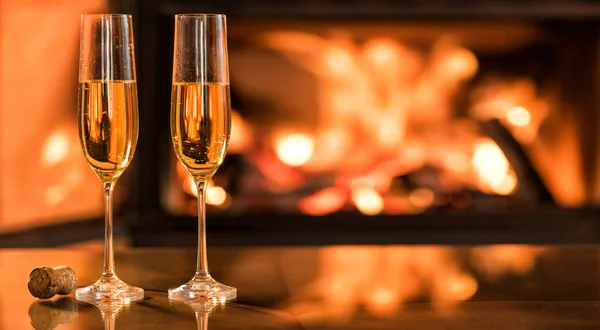 Champán en dos copas en la mesa frente a la chimenea en llamas . — Foto de Stock