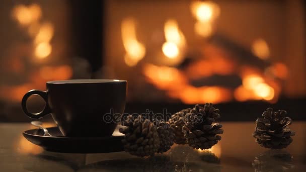 Tapa de café en la mesa frente a la chimenea en llamas . — Vídeos de Stock