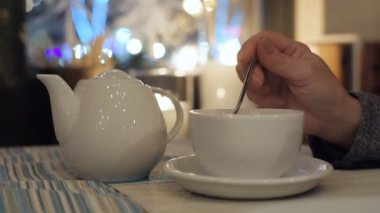Beyaz demlik ve Kupası bir tablo şehir Cafe. Kadın kupa çay kaşığı ile kıpırdanırken..