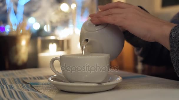 Zblízka ženské ruky nalitím horký čaj z konvice v bílé cup. 