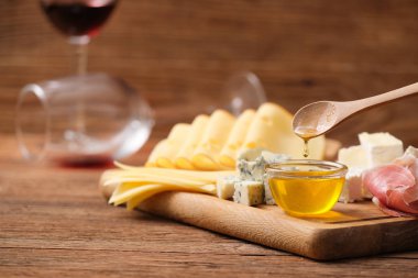 Kaşıkla damlayan bal damlaları. Tahta üzerinde çeşitli peynirler..