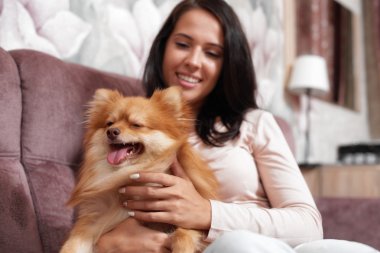 kanepede oturan genç kadın ve köpek tutar.