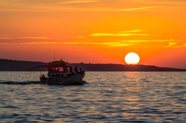 Küçük tekne silueti ile deniz üzerinden günbatımı