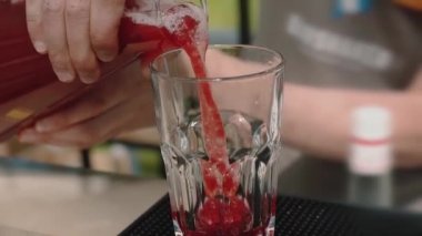 Ağır çekimde buzlu alkollü kırmızı kokteyl döküyorlar..