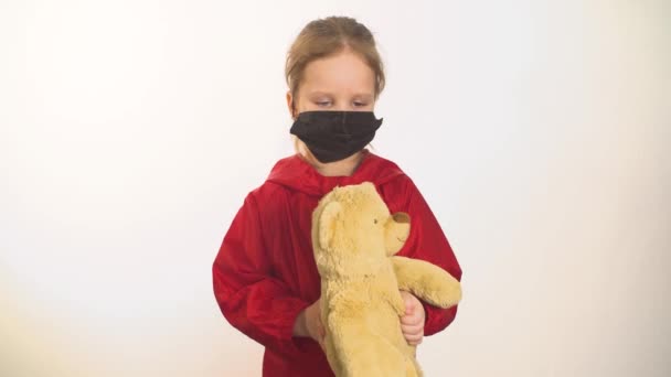 Ребенок держит в руках плюшевого медведя в маске — стоковое видео