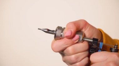Dövme ustası kadın dövme makinesine iğne yerleştirdi. Arka planda yakın plan.