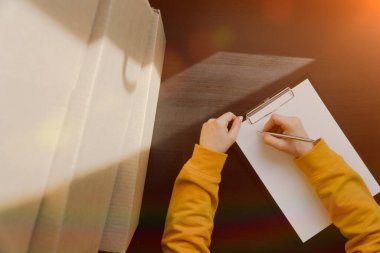 Kız müdür karton kutularda olan şeylerin bir listesini yazar. Deponun envanteri. Üst görünüm, yakın çekim