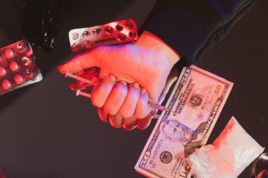 Yakın plan kadın eli hapların ve harcanan paranın arka planında uyuşturucu bulunan bir şırıngayı sıktı. Yetişkin Uyuşturucu Bağımlılığı.