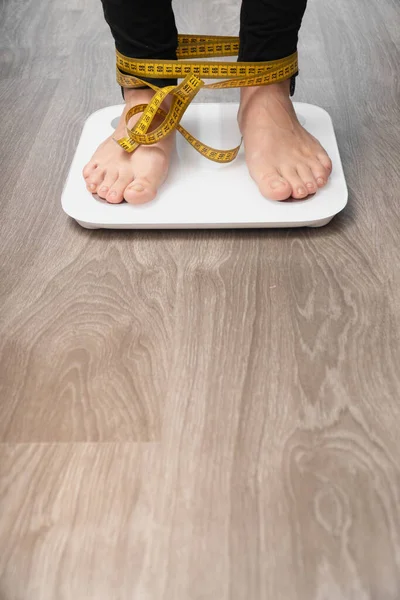 Cropped image of women standing on the scales, on a light background. Feet taped measure.view straight vertical shot.