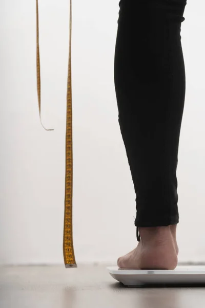 切り取られた女性の足の垂直写真です 手に測定テープを持ってる 自分自身を測定する必要があるという概念は — ストック写真