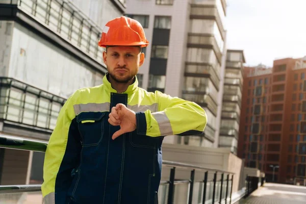 a clean builder shows sincere emotions of indignation. A man in special clothes and a helmet shows dislike against the background of a ready made business center