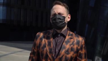 Bir iş merkezinin arka planındaki Avrupalı bir adam tıbbi bir maske takıyor ve etrafına bakıyor. Hüznü geri püskürtme konsepti.