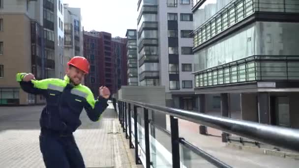 オレンジのヘルメットを着た若い男性の建築家と作業服のジャンプは 建設現場で喜びます とても幸せな労働者 — ストック動画