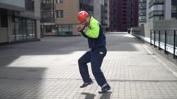 Jonge Vrolijke Bouwer Een Oranje Helm Werkkleding Dansen Een Bouwplaats — Stockvideo