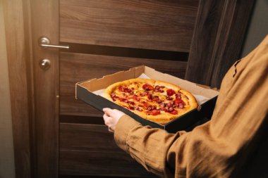 Kadın elleri kapının önünde nefis bir pepperoni pizzasını tutuyor. Ofise yemek servisi..