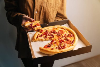 Kadın eli, pepperonili pizzanın ilk dilimini teslimat kutusundan çıkarır. Fast food konsepti.