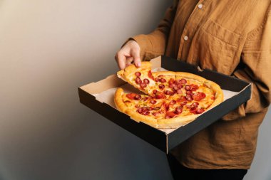 Kadın eli, pepperonili pizzanın ilk dilimini teslimat kutusundan çıkarır. Fast food konsepti.