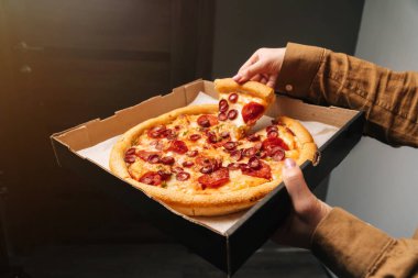 Kadın eli, pepperonili pizzanın ilk dilimini teslimat kutusundan çıkarır. Fast food konsepti.