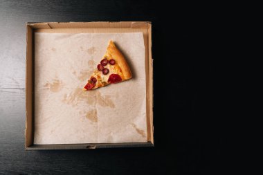 Son dilim pepperonili pizzayı karton bir karton kutunun içinde, karanlık bir arka planda. Yukarıdan görüntüle.