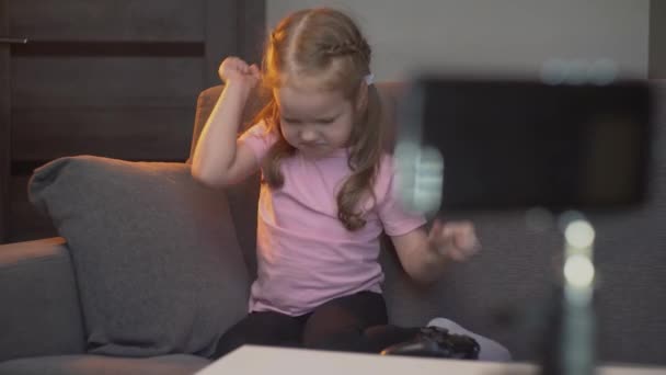 一个白人小女孩坐在沙发上玩视频游戏 孩子生气了 在玩耍的时候挥动着双臂 — 图库视频影像