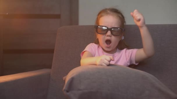 女の子は目の上に3Dメガネをかけ 恐怖の中で漫画を見て 映画を見ながら恐怖の中で手を振っています 子供の目に衝撃の概念 — ストック動画