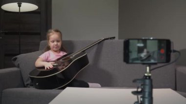 Kamerada akustik gitardan bahseden küçük, güzel bir beyaz çocuk blogcu, görüşünü abonelerle paylaşıyor. vlog günlük kavramı.