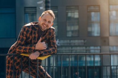 Genç beyaz bir adam, güzel bir arka plan olan evlere pençe işareti yapıyor. Takım elbiseli başarılı bir iş adamı konsepti..