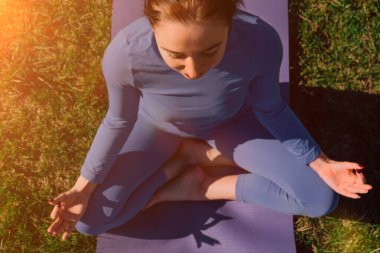 Üst Manzara Genel Planı. Eller namaste 'ye yakın. Genç beyaz kız parkta yoga meditasyonu yapıyor..