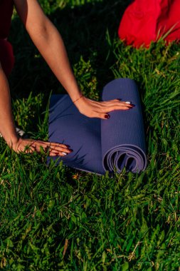 dikey çerçeveli kadınların elleri yeşil çimlerin üzerine bir spor minderi serer. Açık hava sporu konseptinde..