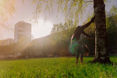 Genç bir sporcu kız bir ağacın üzerinde destekle kollarında duruyor. Sokak eğitimi kavramı. Spor öğrenen kadın.