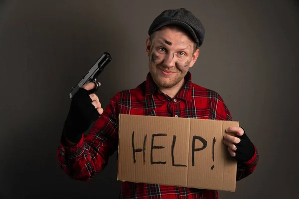 young thug holding a gun and a sign asking for help. The concept of unemployed hooliganism.