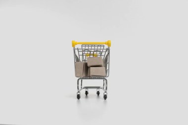 İçinde karton kutular olan küçük bir sepet. İnternet üzerinden mal satma kavramı izole edilmiş beyaz bir zemin üzerinde.