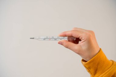 Kadın elinin termometresi ve arka planında basit bir manikür var. Hastalık sırasında ateş ölçün.