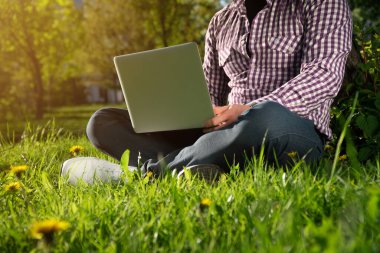 Yukarıdan bakıldığında, genç serbest çalışan güneşli bir günde bir ağacın altında oturuyor. Bir dizüstü bilgisayarla çalışıyorum. Parkta online iş kavramı