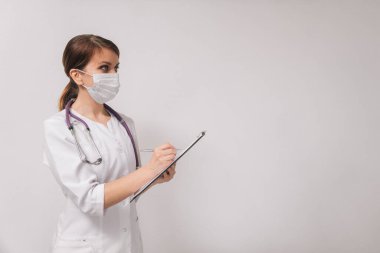 Kadın bir doktor hastaya teşhis koyar. Tıbbi maskeli doktor ve klinikteki beyaz cüppeli doktor..