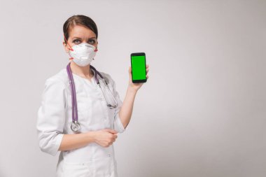 Arka planda beyaz önlüklü güzel bir bayan doktor yeşil ekranlı bir akıllı telefon tutuyor. Mobil uygulama için izole arkaplan..