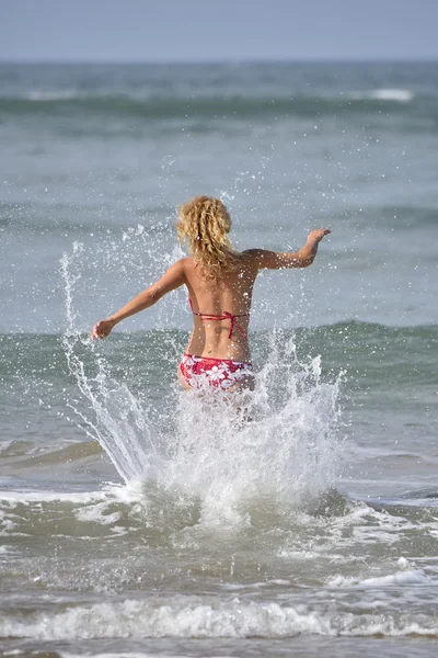 Woman in bikini running into the water — Stockfoto