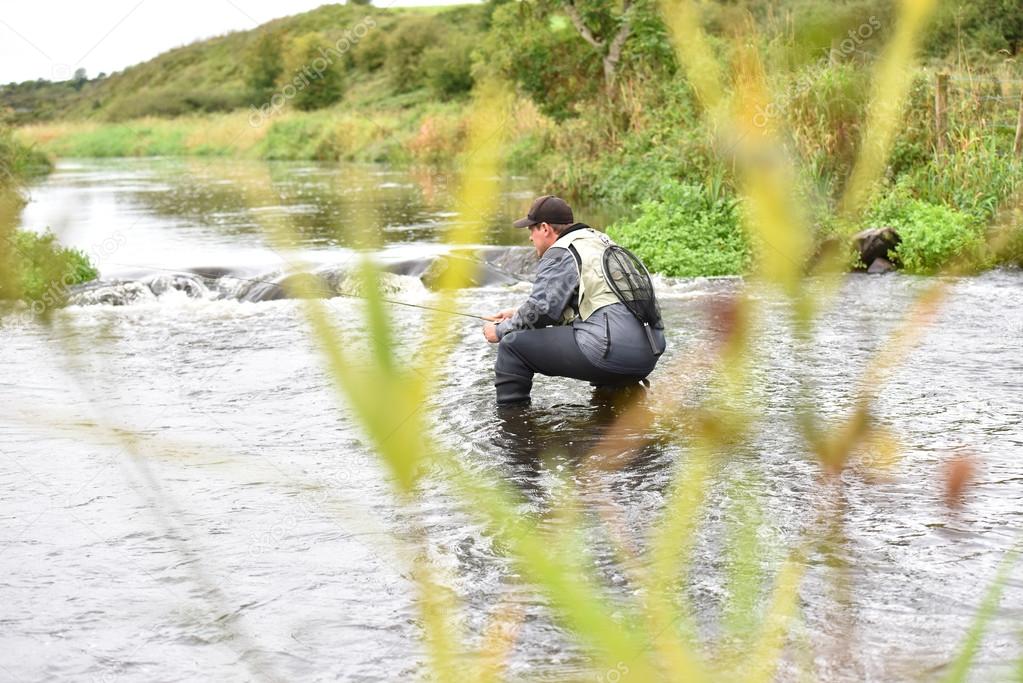 Fly-fisherman knelt in river