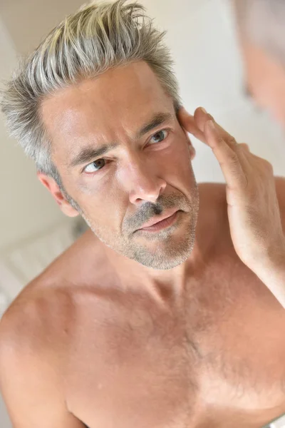 Man in front of mirror applying cream — Stock Photo, Image